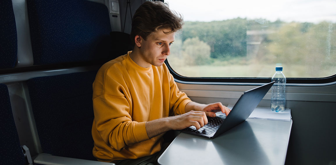 Young male freelancer in orange sweatshirt working on laptop in