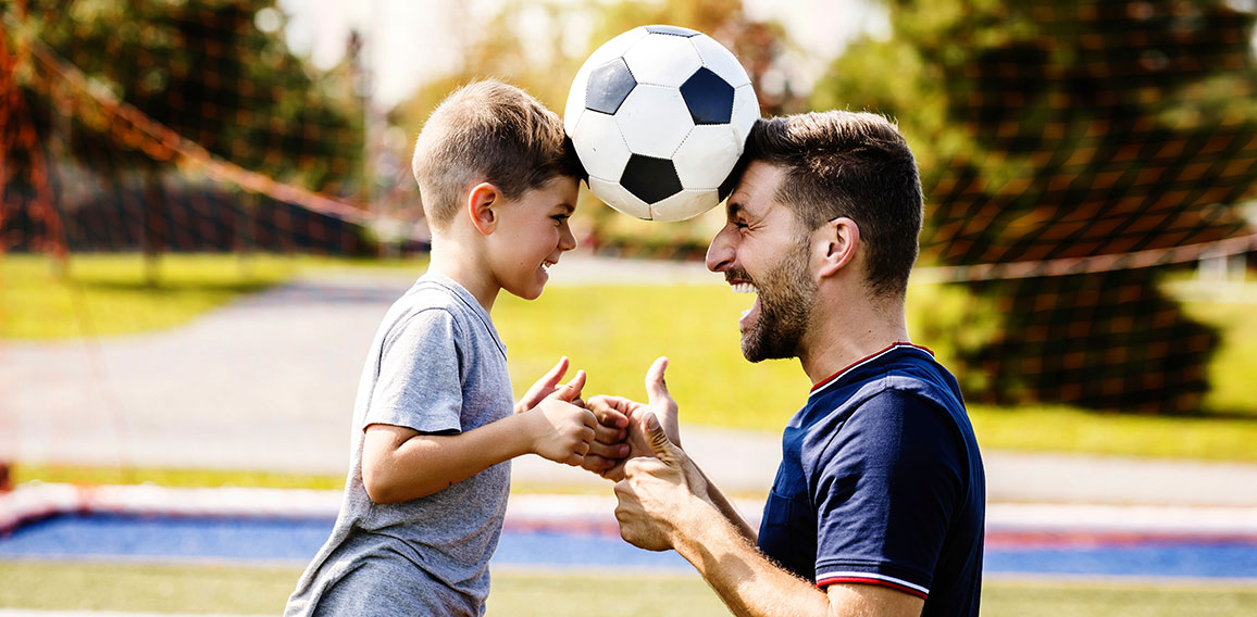 man with child playing football outside on field