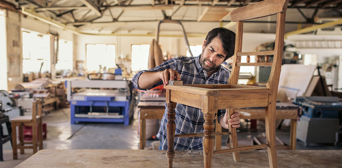 Furniture maker sanding a chair on workshop bench