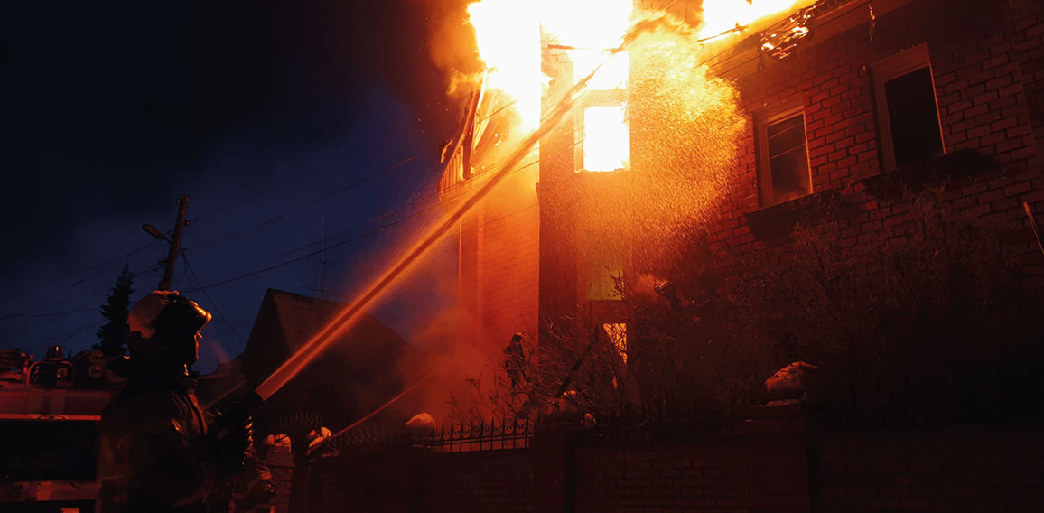 The roof of the house is on fire. The residential building burn, village. Firefighters put out a fire from the crane from above. Smoke and sparks.