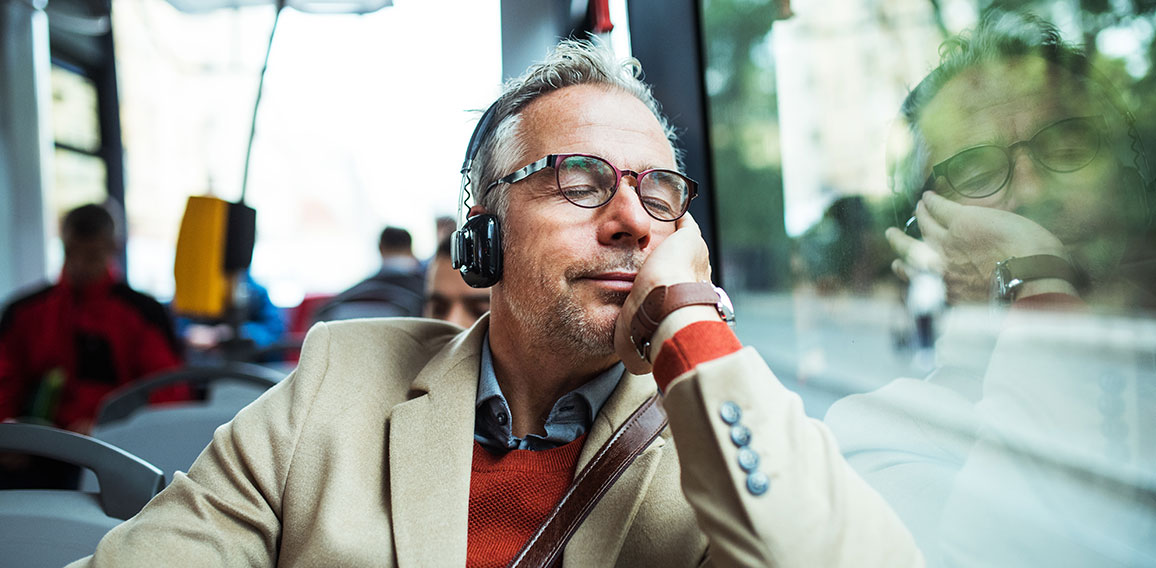 Mature tired businessman with heaphones travelling by bus in city.