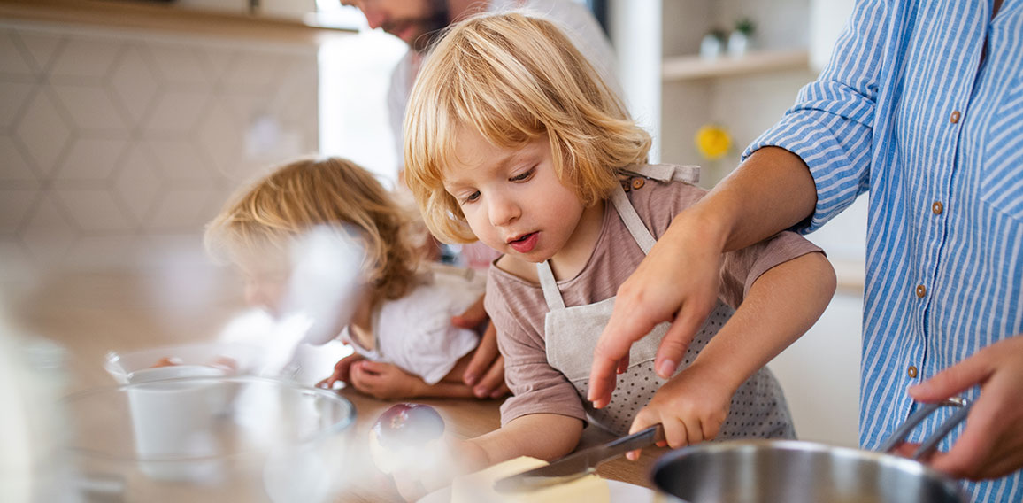 Young family with two small children indoors in kitchen, preparing food.