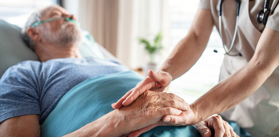 Unrecognizable female doctor examining senior man in bed in hospital.