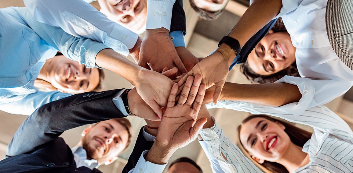 Coworkers Standing In Circle Holding Hands During Meeting In Office