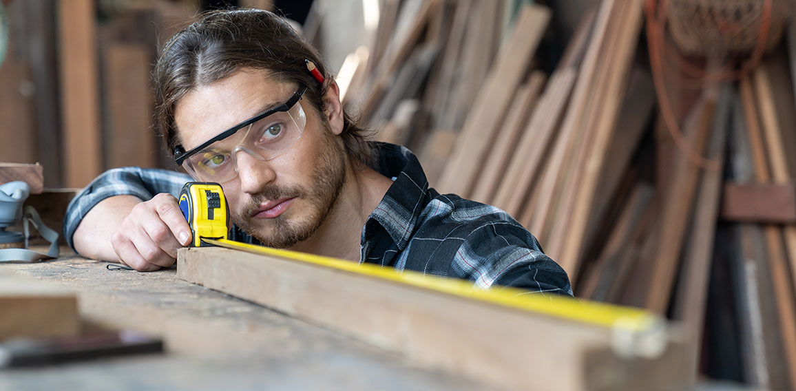 Male carpenter using measuring tape at the carpentry workshop. J