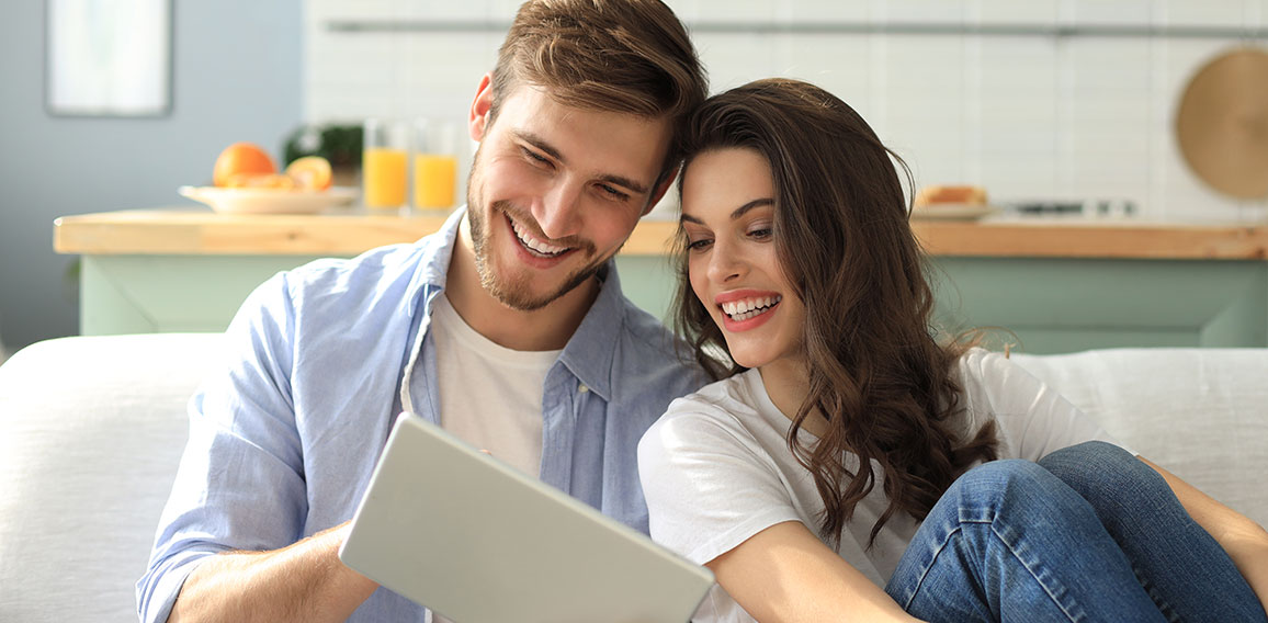 Young couple watching media content online in a tablet sitting on a sofa in the living room.