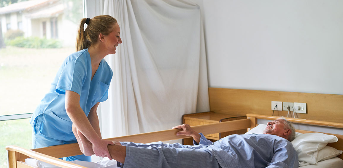 Nurse lifting legs of elderly man lying in bed