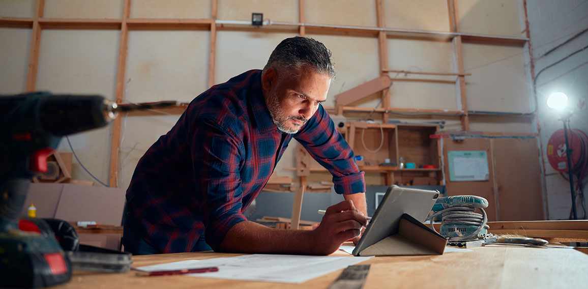 Mid adult man writing with digitized pen on digital tablet next to tools in woodworking factory