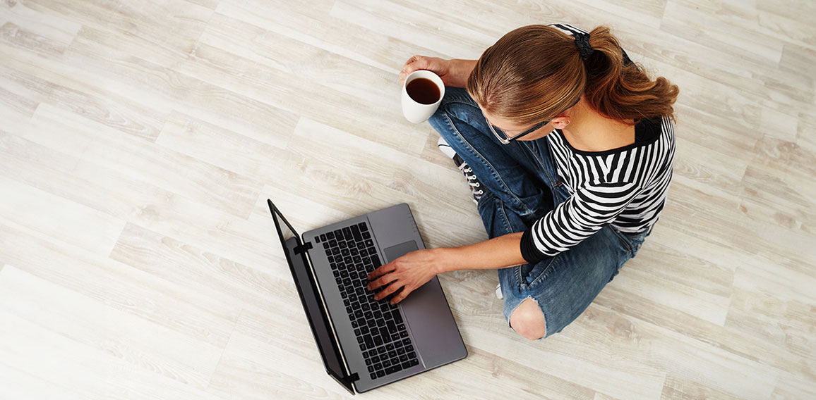 Young woman with coffee mug sitting on the floor with laptop. Co