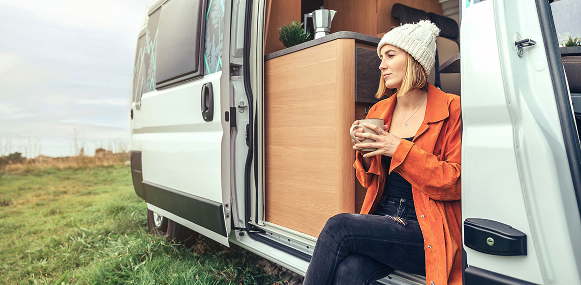 Woman drinking coffee sitting at the door of a campervan