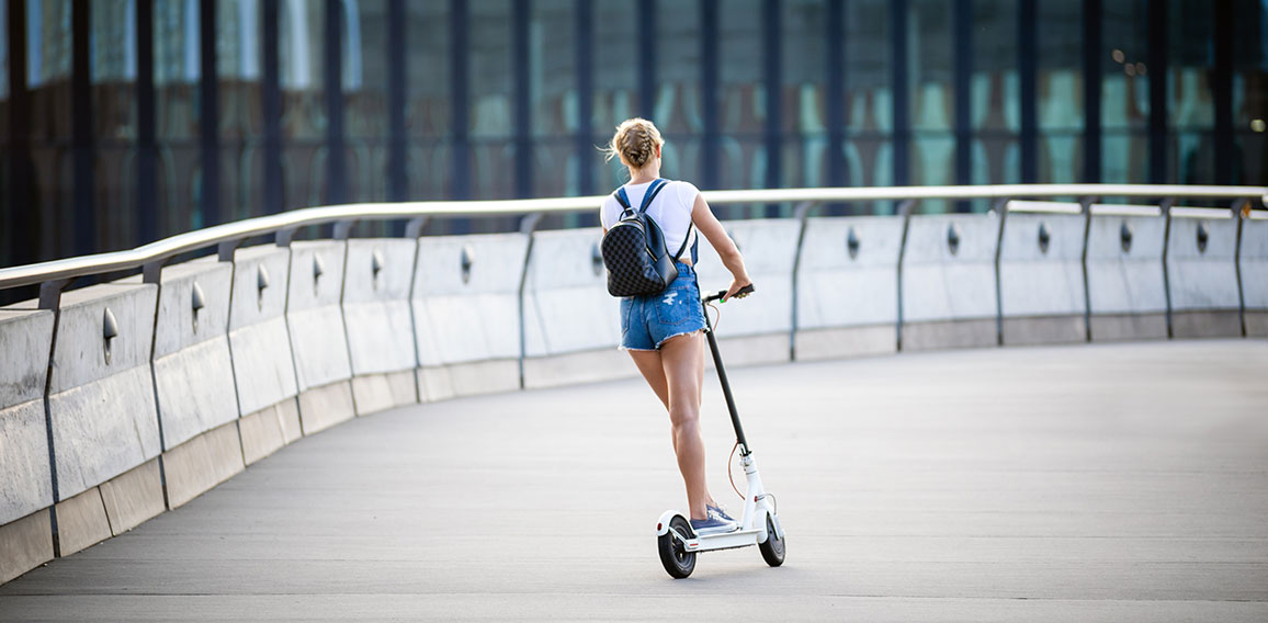 Back view of woman riding an electric scooter on modern buildings background