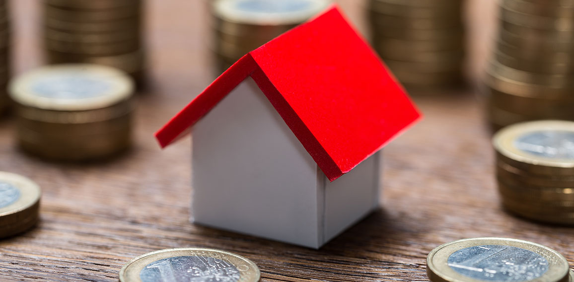 House Model Amidst Coins At Table