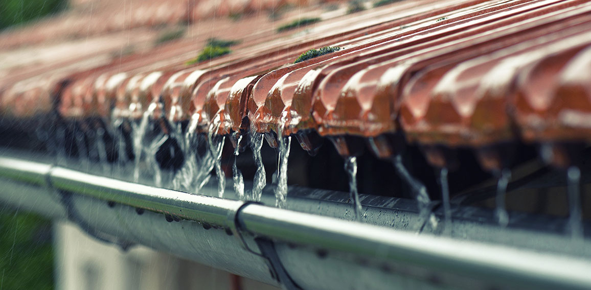 Drops of water flow into the eaves on the house in the rain.