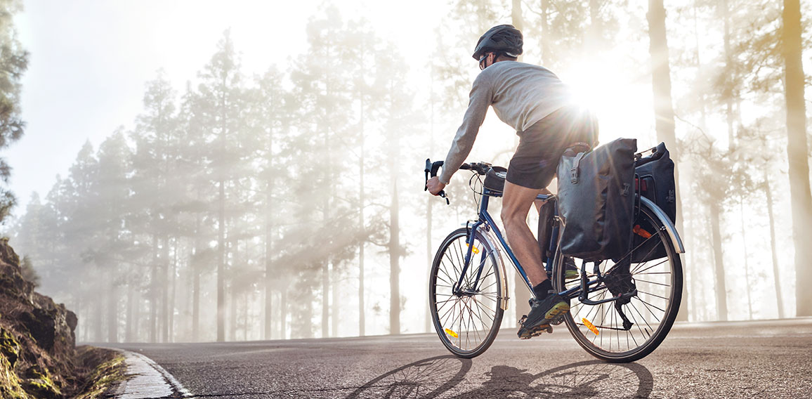 Cyclist on a bicycle with panniers riding along a foggy forest r