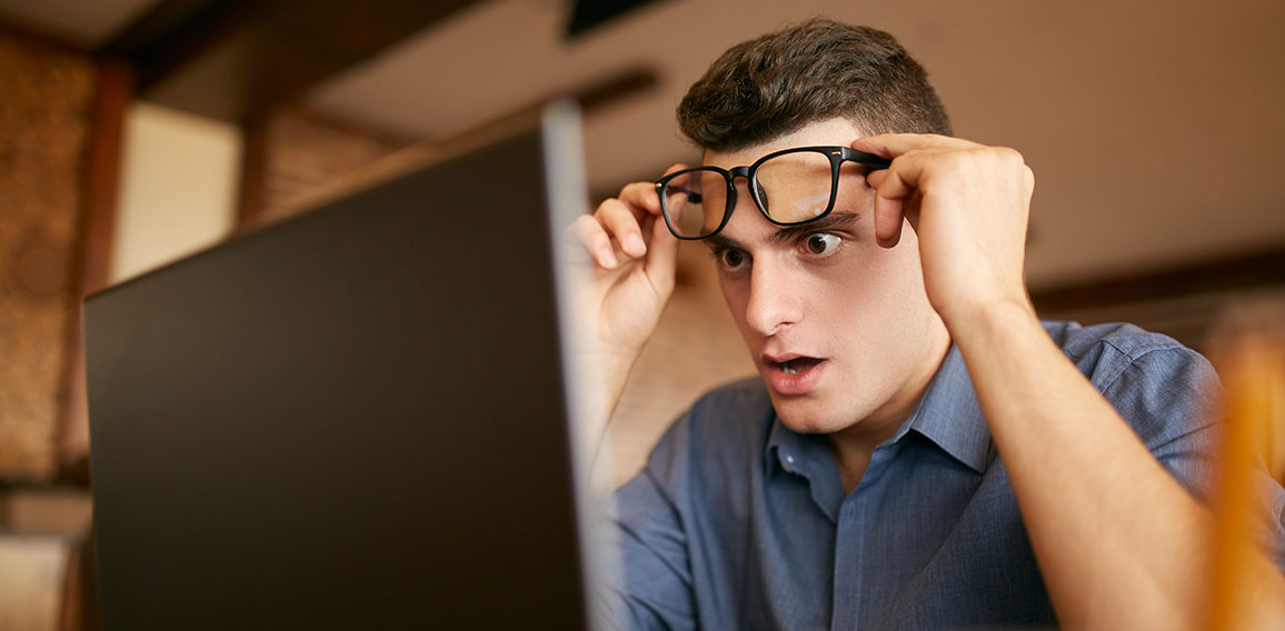 Shocked freelancer hipster man looks to laptop screen and can not believe unpleasant news. Pop-eyed frightened businessman trader raises one's glasses above his eyes. Trader monitoring stock exchange