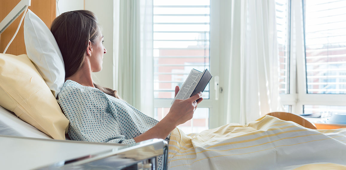 Patient in hospital room looking out of the window from bed