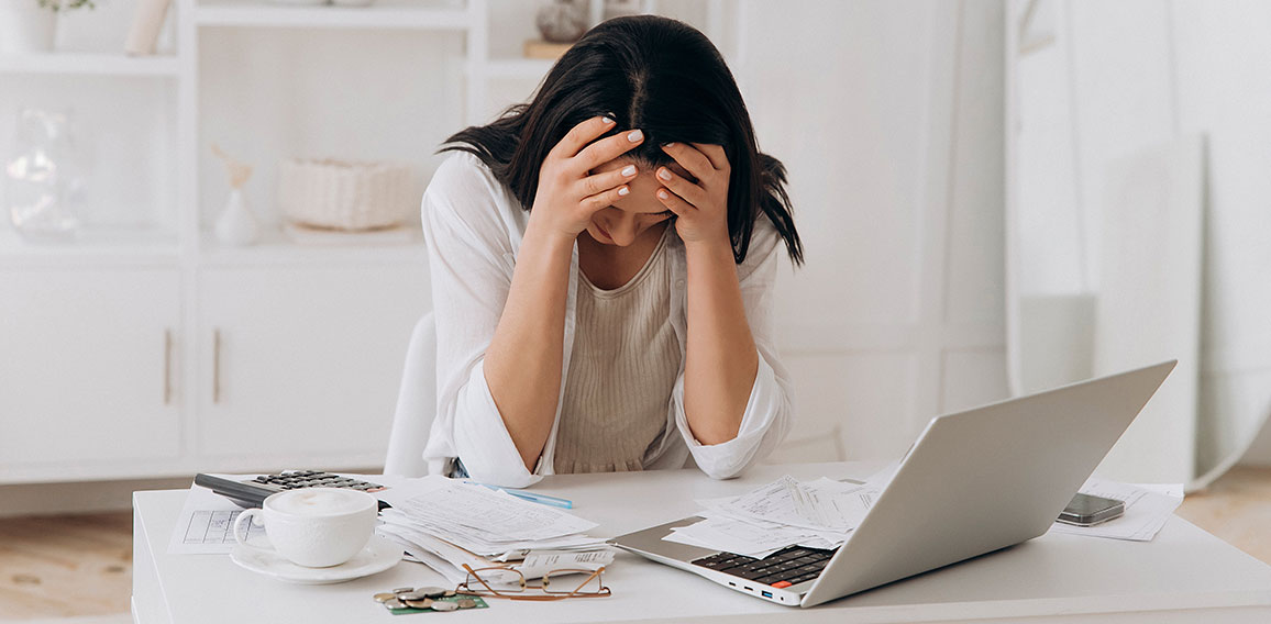 Desperate young woman holds head in hands, feeling overwhelmed by financial paperwork at white office desk, struggling with bills, taxes, and credit management, bankruptcy concept, mental health