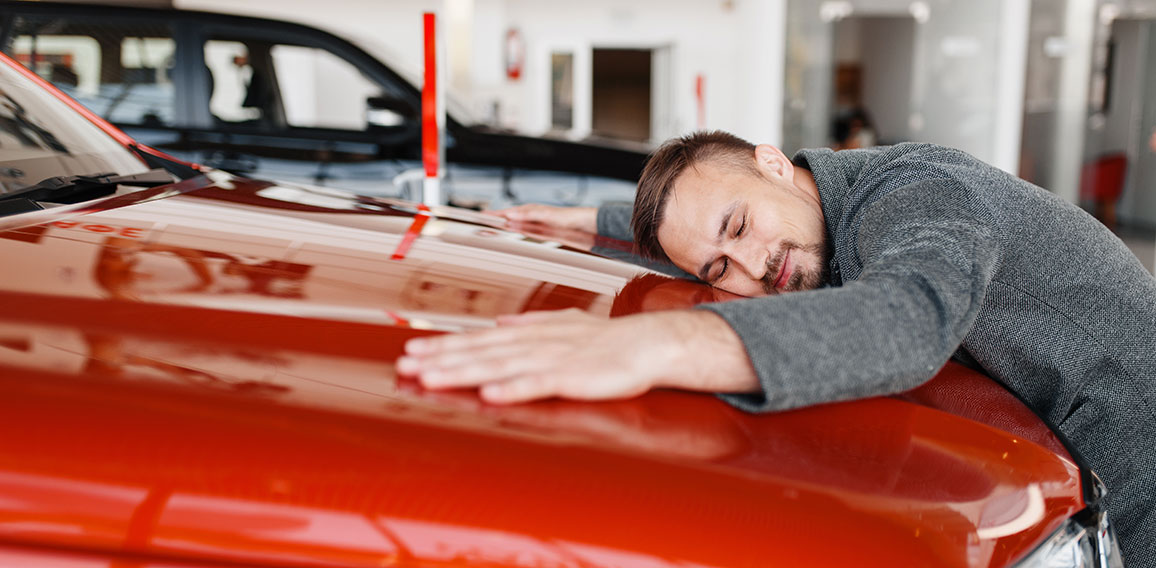 Man lying on the hood of new car in showroom