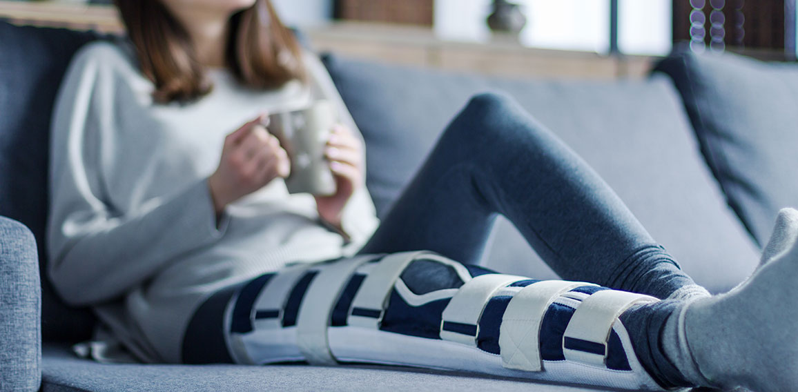 Smiling brunette girl with broken leg is sitting on couch sofa,