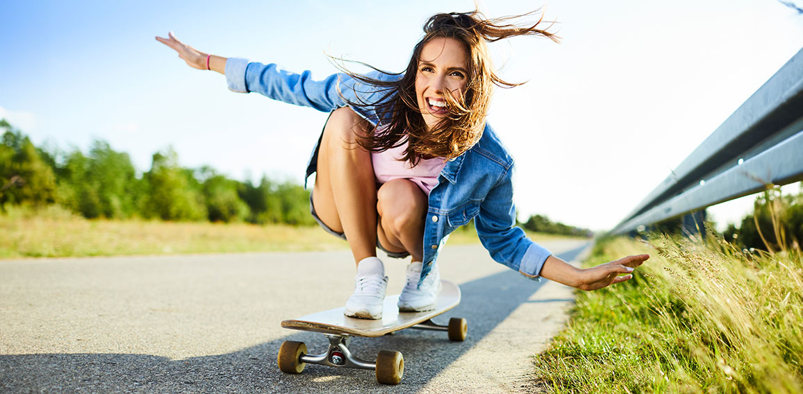 Cheerful young woman riding longboard in countryside setting