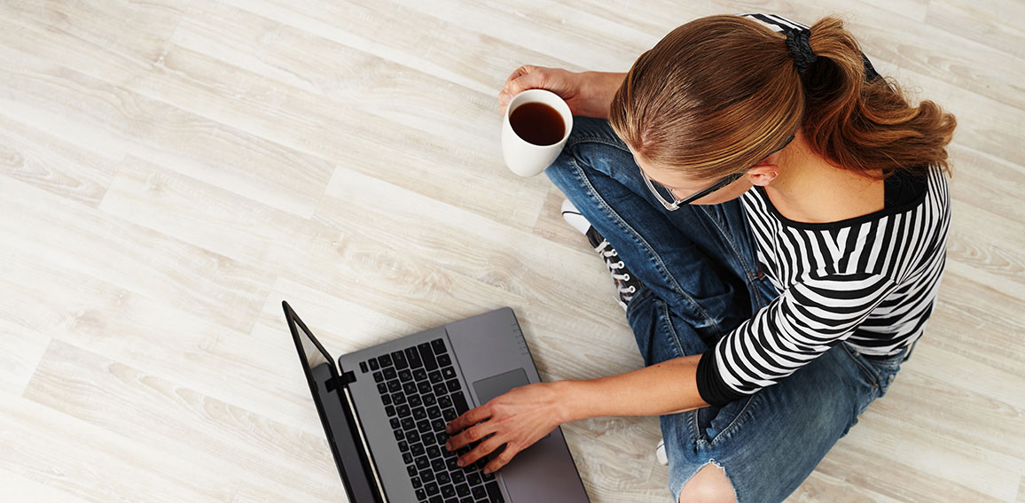 Young woman with coffee mug sitting on the floor with laptop. Co