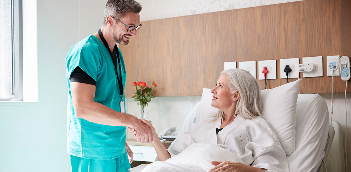 Surgeon Visiting And Shaking Hands With Mature Female Patient In Hospital Bed