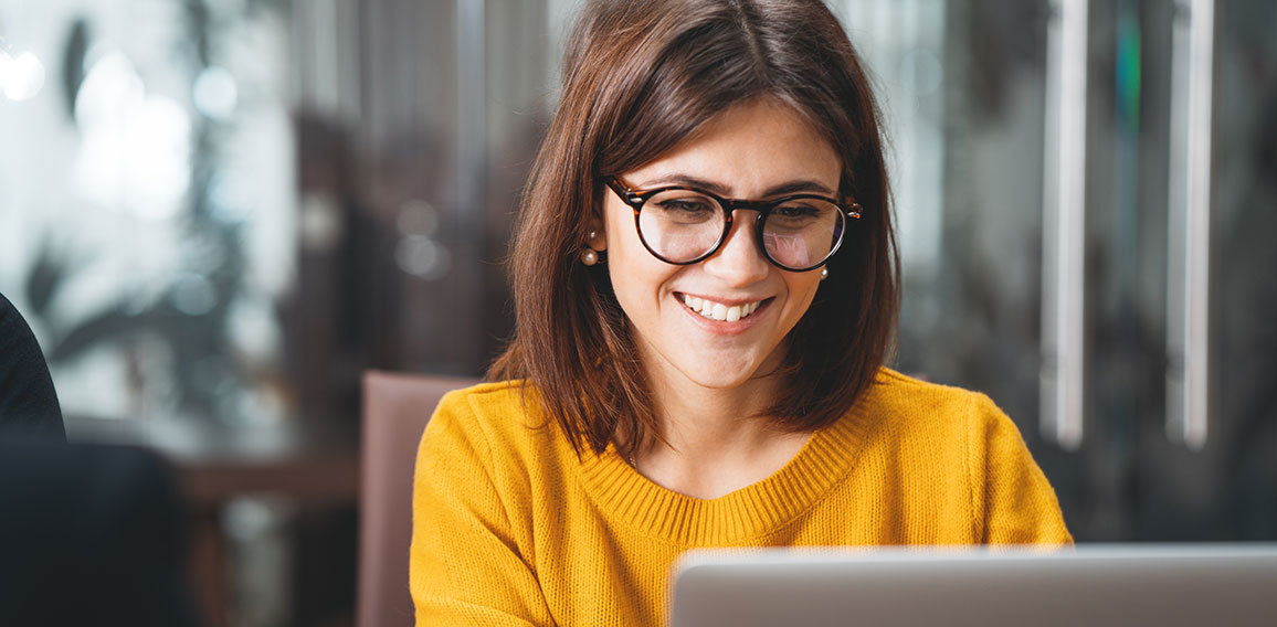 Portrait of happy business woman wearing glasses at workplace in office. Young handsome female worker using modern laptop