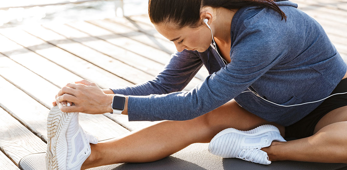 Fitness woman make stretching exercises at the beach outdoors listening music with earphones.